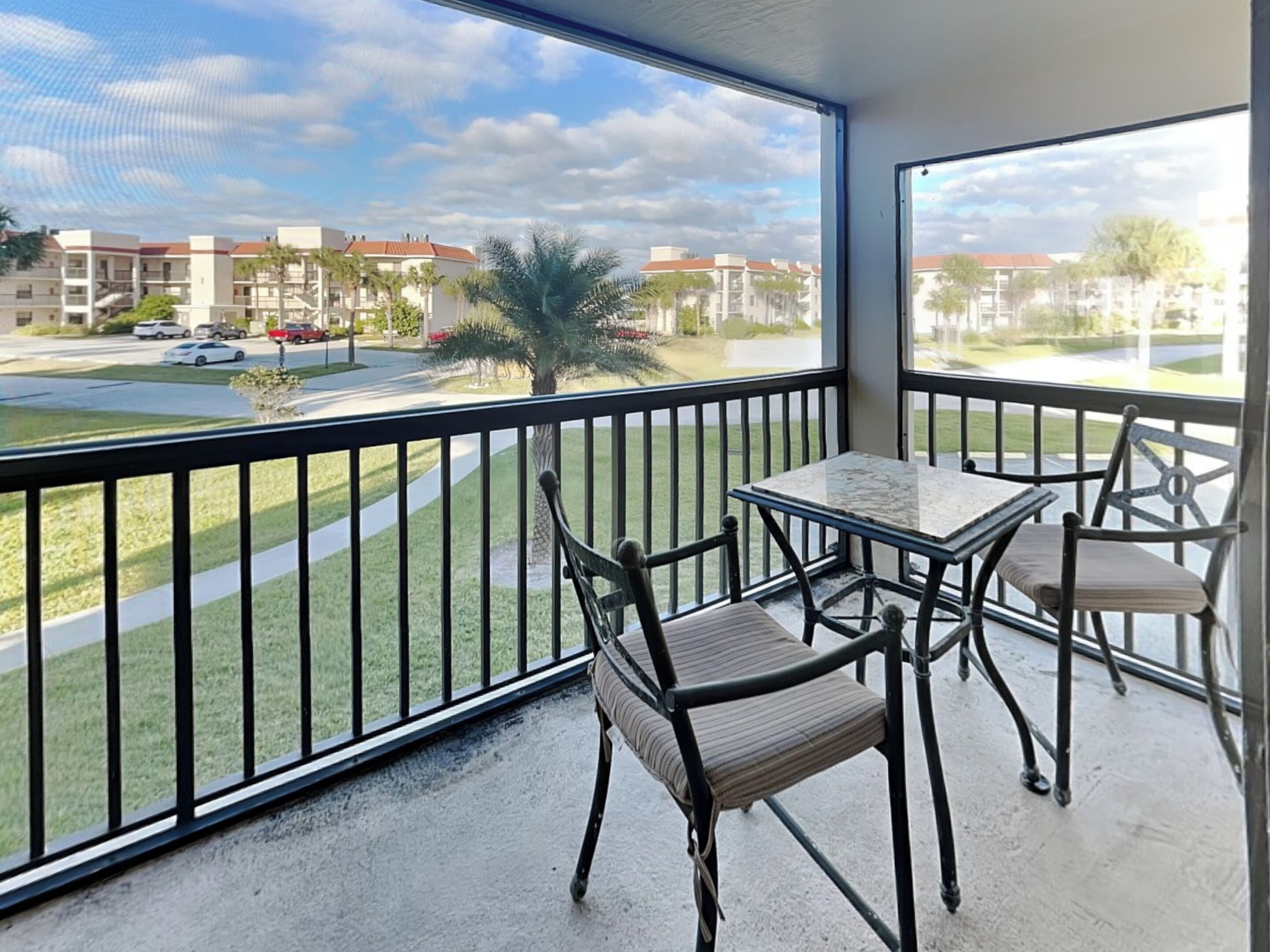 A balcony with a table and chairs, overlooking a residential area with buildings and a road.