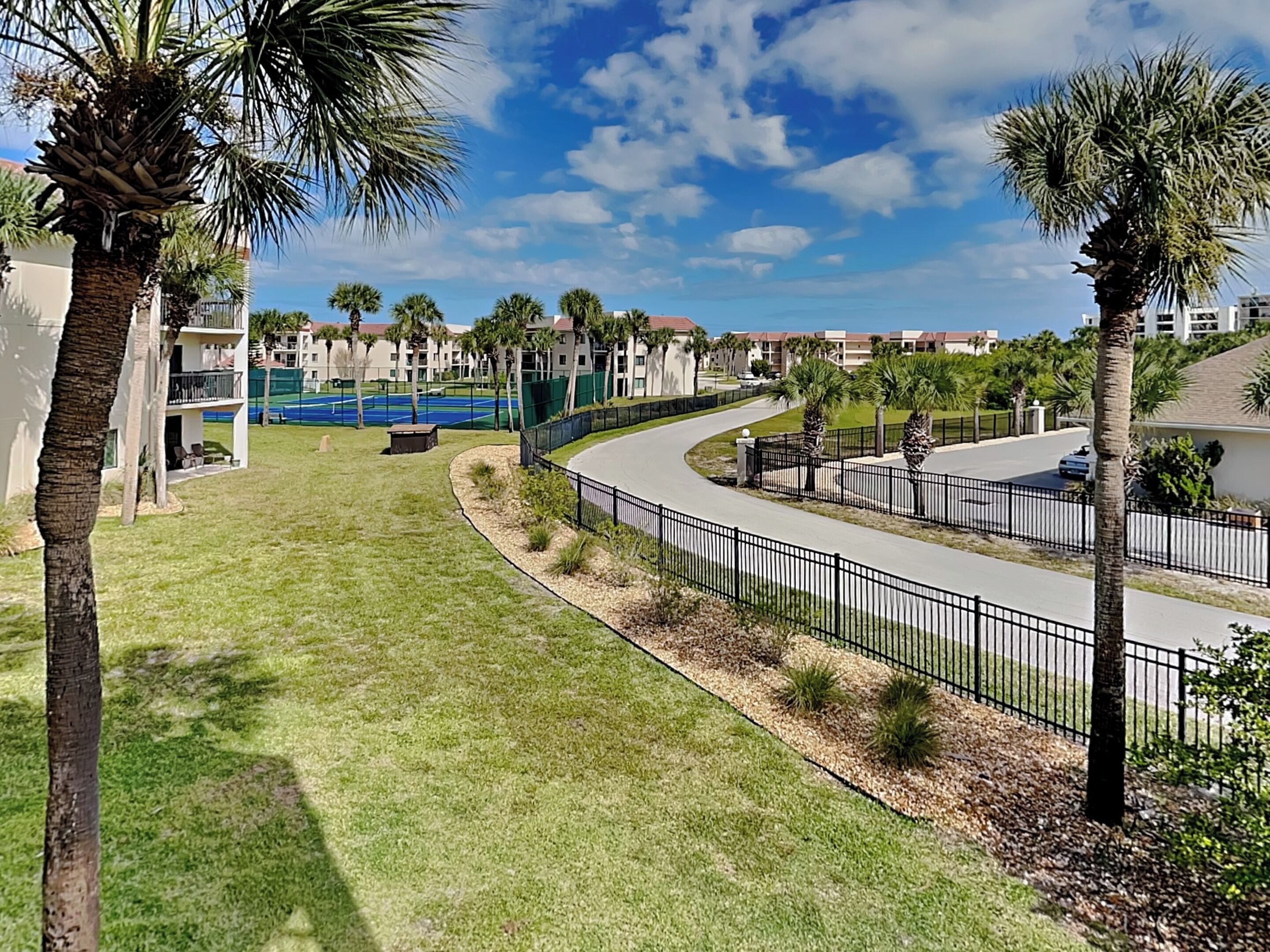 A residential area with a curved road, palm trees, and a tennis court.