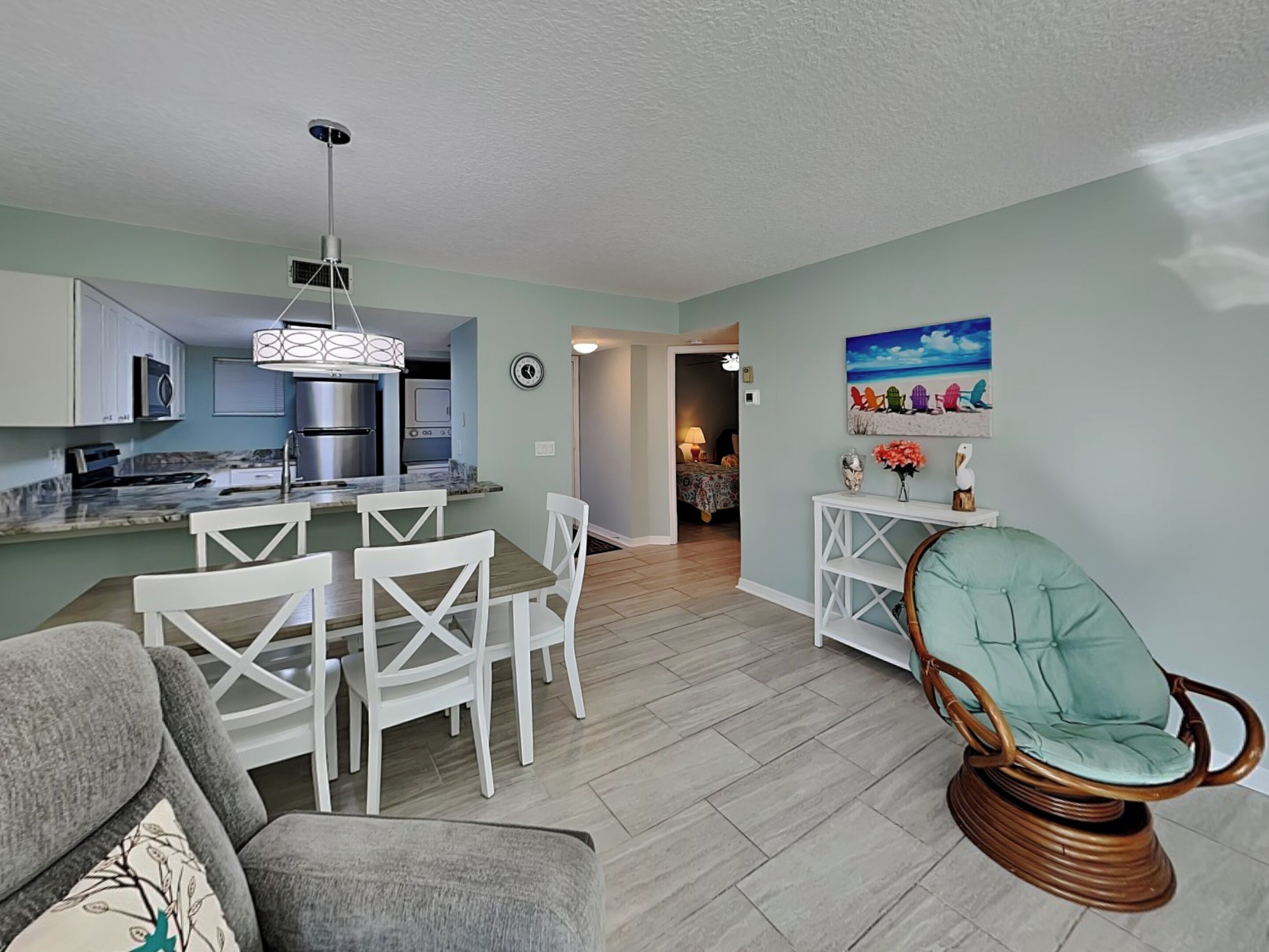 A modern living room with a dining area, kitchen, and a hallway leading to a bedroom.