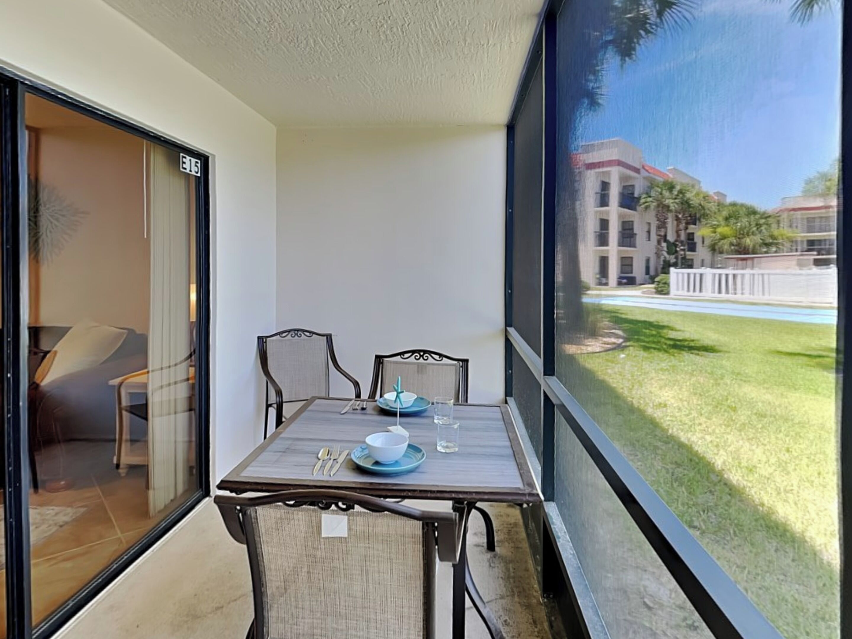Un balcon avec une table dressée pour deux personnes, une chaise et une vue sur un immeuble et une pelouse.