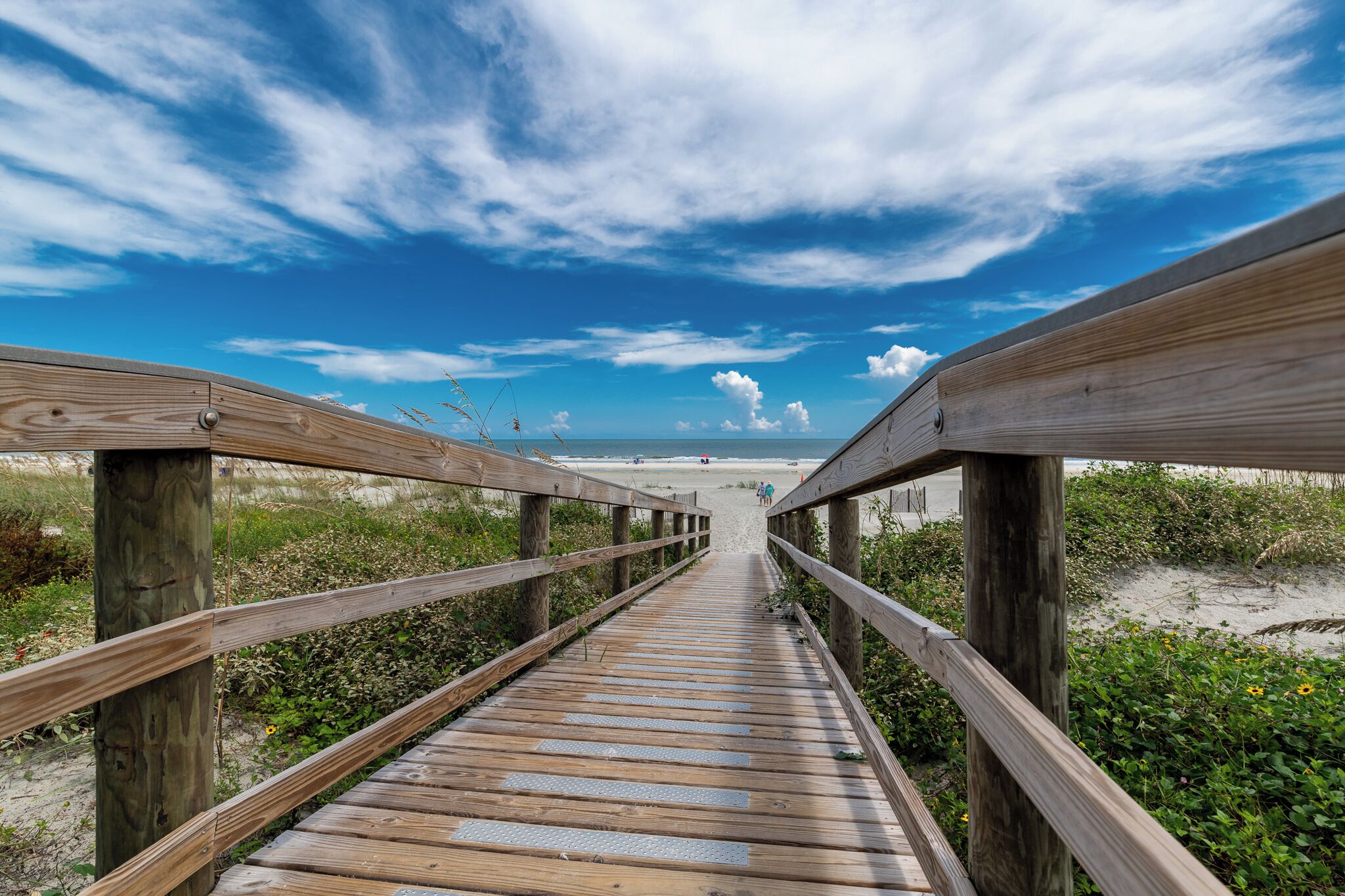 A wooden boardwalk leading to a beach with a clear sky.