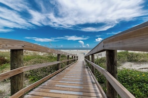 Une promenade en bois menant à une plage, avec un ciel dégagé.