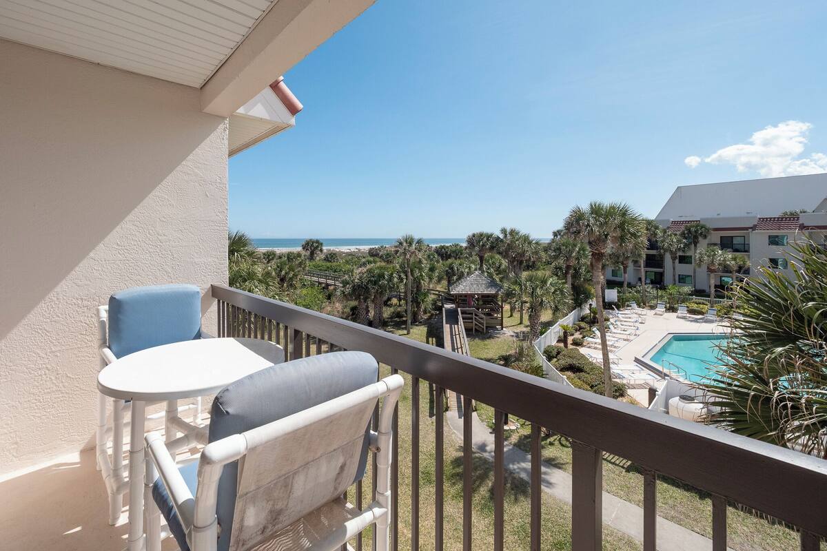 Ein Balkon mit Blick auf ein Schwimmbad, Palmen und einen Strand.