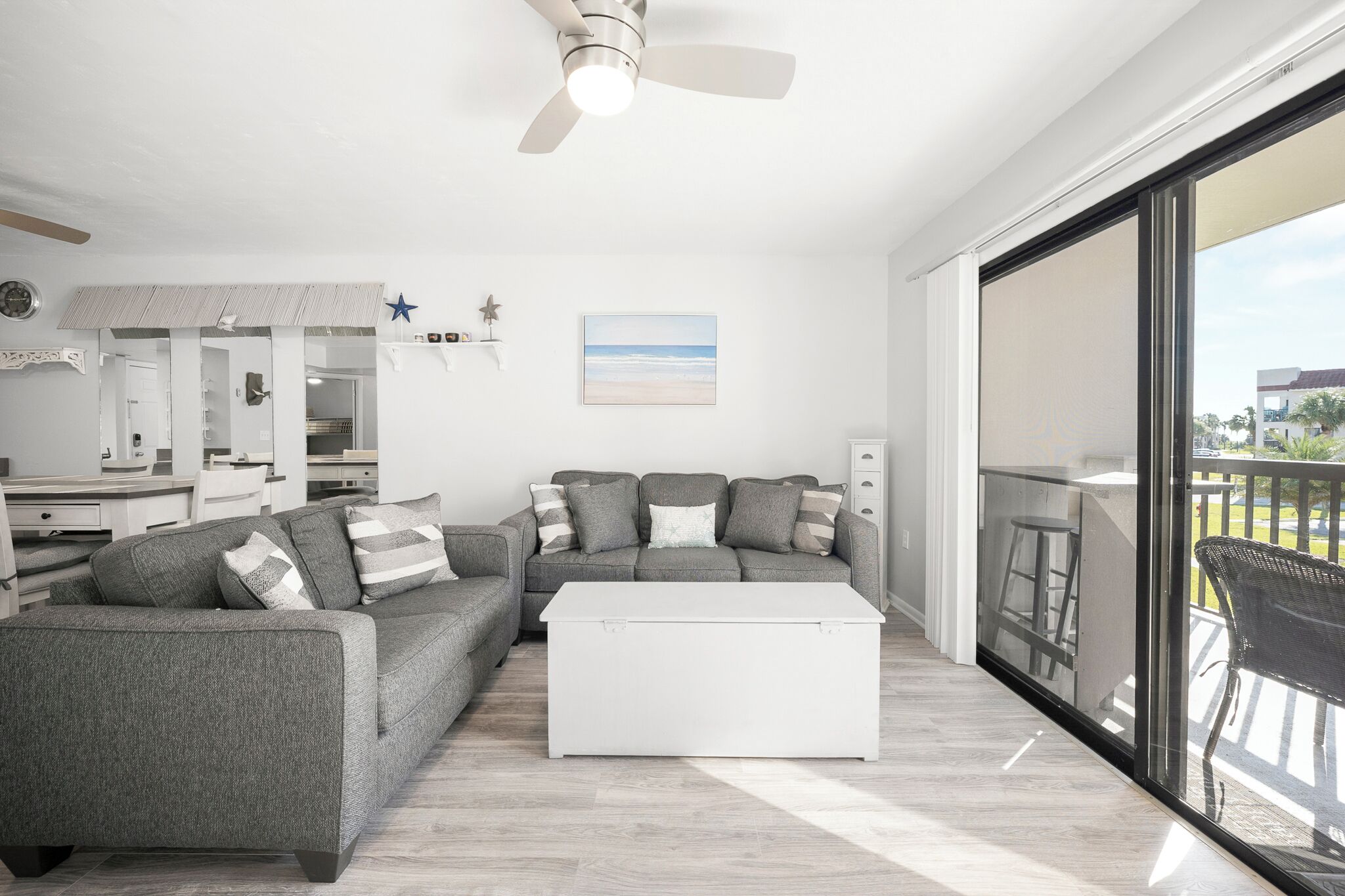 A modern living room with a grey sofa, white coffee table, and a large sliding glass door leading to a balcony.