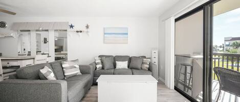 A modern living room with a grey sofa, white coffee table, and a large sliding glass door leading to a balcony.