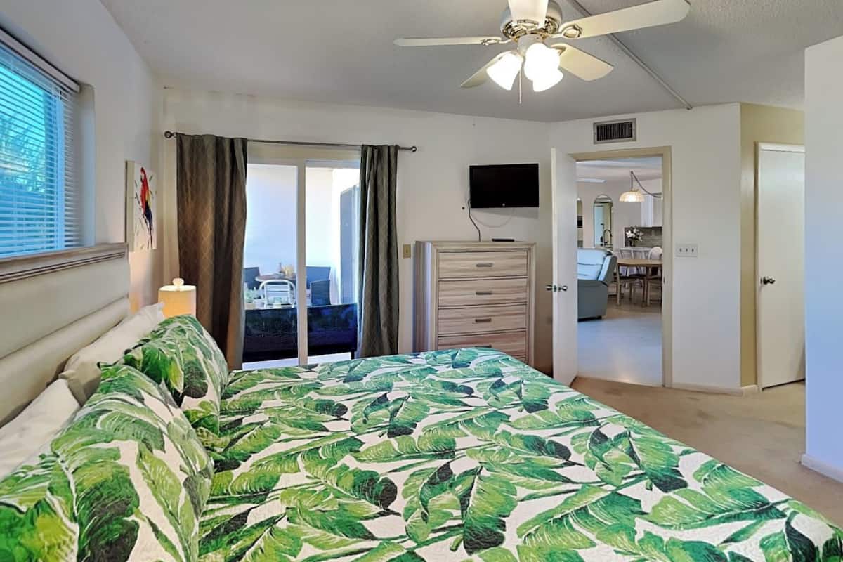 Ein Schlafzimmer mit einem Bett, einem Deckenventilator, einem Fernseher und Blick auf den Balkon.