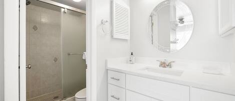 Une salle de bain avec une douche à parois de verre, un miroir rond et des meubles de rangement blancs.