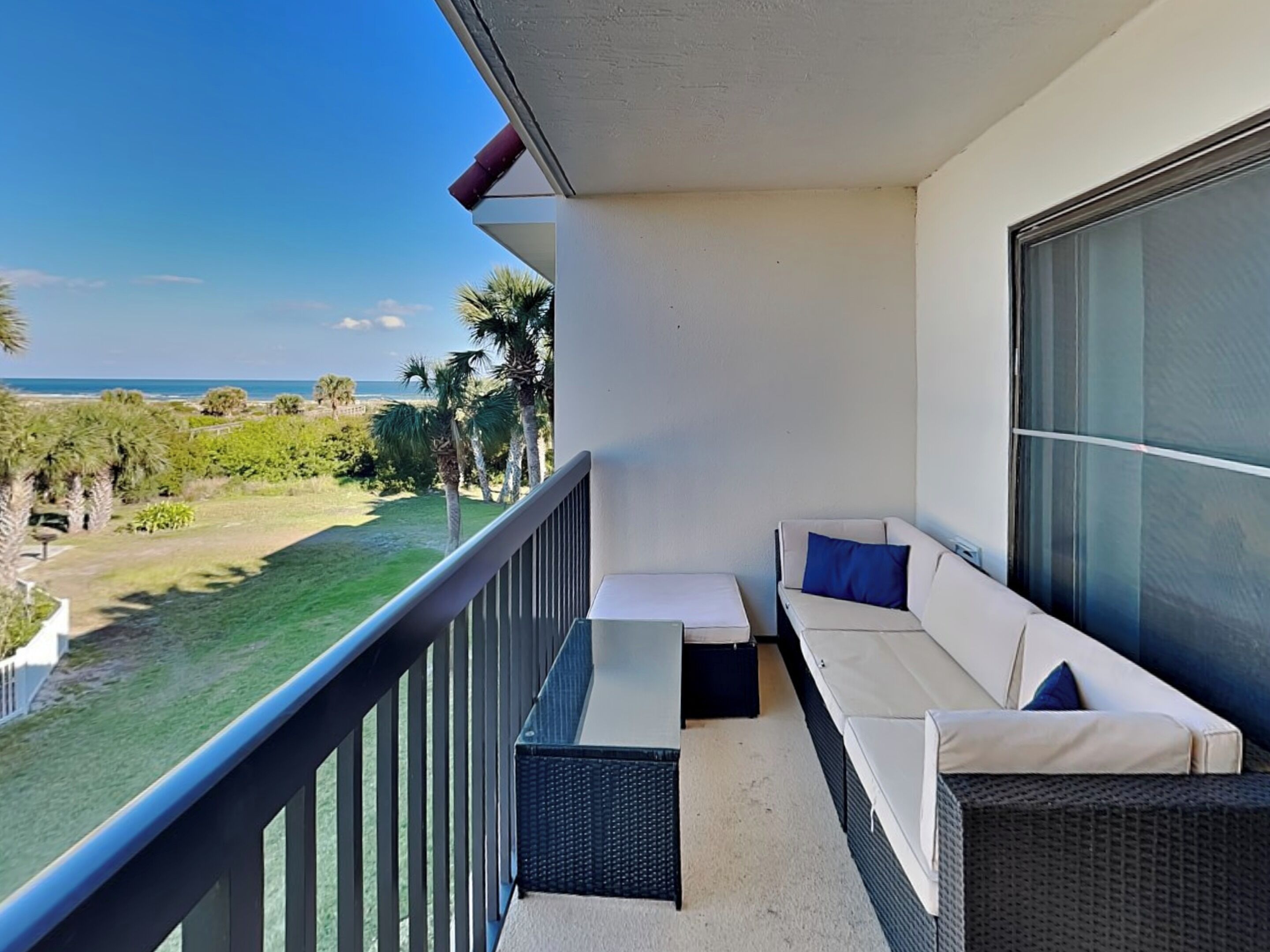 A balcony with a view of the ocean, a white sofa with blue cushions, and a small table.