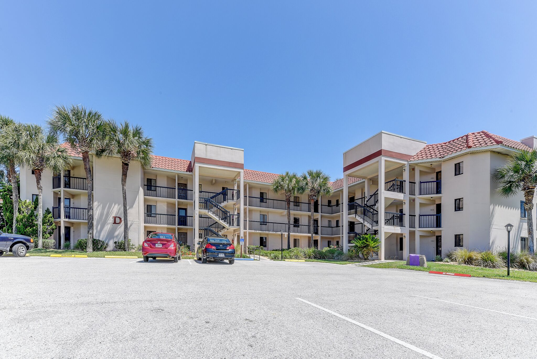 A multi-story hotel with balconies, palm trees, and a parking lot.