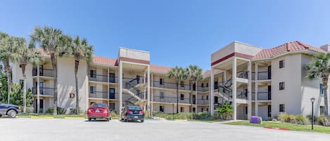 A multi-story hotel with balconies, palm trees, and a parking lot.