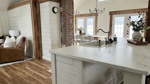 A kitchen with a large island, a brick wall, and a wooden ceiling. - Birchwood Cottage, 200ft of Lake Beach-Fully flat lot -Private Driveway (Branchport)