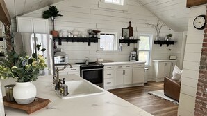 A kitchen with white cabinets, a marble countertop, and a brick wall. - Birchwood Cottage, 200ft of Lake Beach-Fully flat lot -Private Driveway (Branchport)