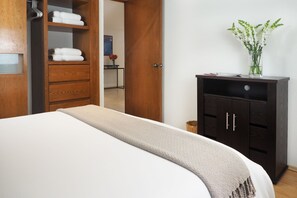Hotellihuone, jossa on sänky, puinen vaatekaappi ja pieni työpöytä, jonka päällä on maljakko täynnä kukkia.