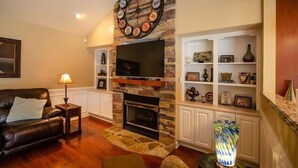 Ein Wohnzimmer mit Kamin aus Stein, einer Wanduhr, einem Flachbildfernseher und einem Bücherregal.