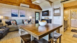 A cozy cabin interior with a wooden dining table, sofa, and a TV mounted on the wall. - What A View | Ellijay, GA (Ellijay)