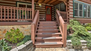 A wooden staircase leading to a porch with a stone wall and greenery.