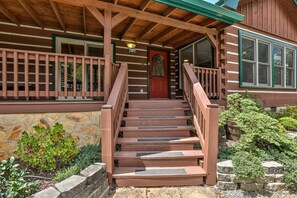 A wooden staircase leading to a porch with a stone wall and greenery.