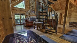 A wooden cabin interior with a spiral staircase, a fireplace, and a view of the outdoors.