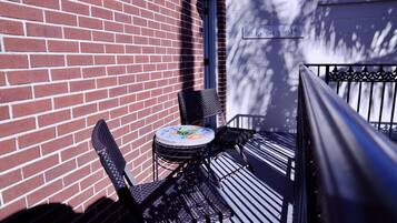 A small outdoor seating area with a table and chairs, a brick wall, and a metal railing.