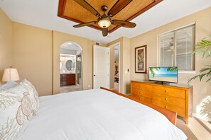Quarto com cama, televisão, ventoinha no teto, cômoda e janela com persianas.