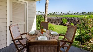 A covered patio with a table set for four, overlooking a landscaped garden and a view of a golf course.