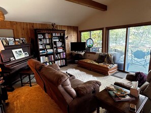 Un salon chaleureux avec un piano, des canapés en cuir, une bibliothèque et une grande fenêtre donnant sur l’extérieur.