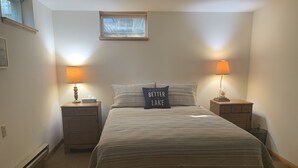 A bedroom with a bed, two bedside tables, a window, and a bench. - Round Lake's Happy Swimmers 1970's-80's Retro Cottage (Waupaca)