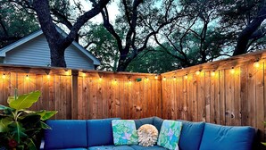 A blue sectional sofa with floral cushions, a wooden deck, and string lights against a wooden fence. - Executive Housing — Medical • Corporate • Projects (San Antonio)