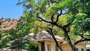 A historic stone building with a large tree in front, a covered porch, and a clear blue sky. - Executive Housing — Medical • Corporate • Projects (San Antonio)