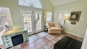 A living room with a beige sofa, a small side table, a lamp, and a bench. There are two doors leading outside, one with a window and the other with a mirror. - Executive Housing — Medical • Corporate • Projects (San Antonio)
