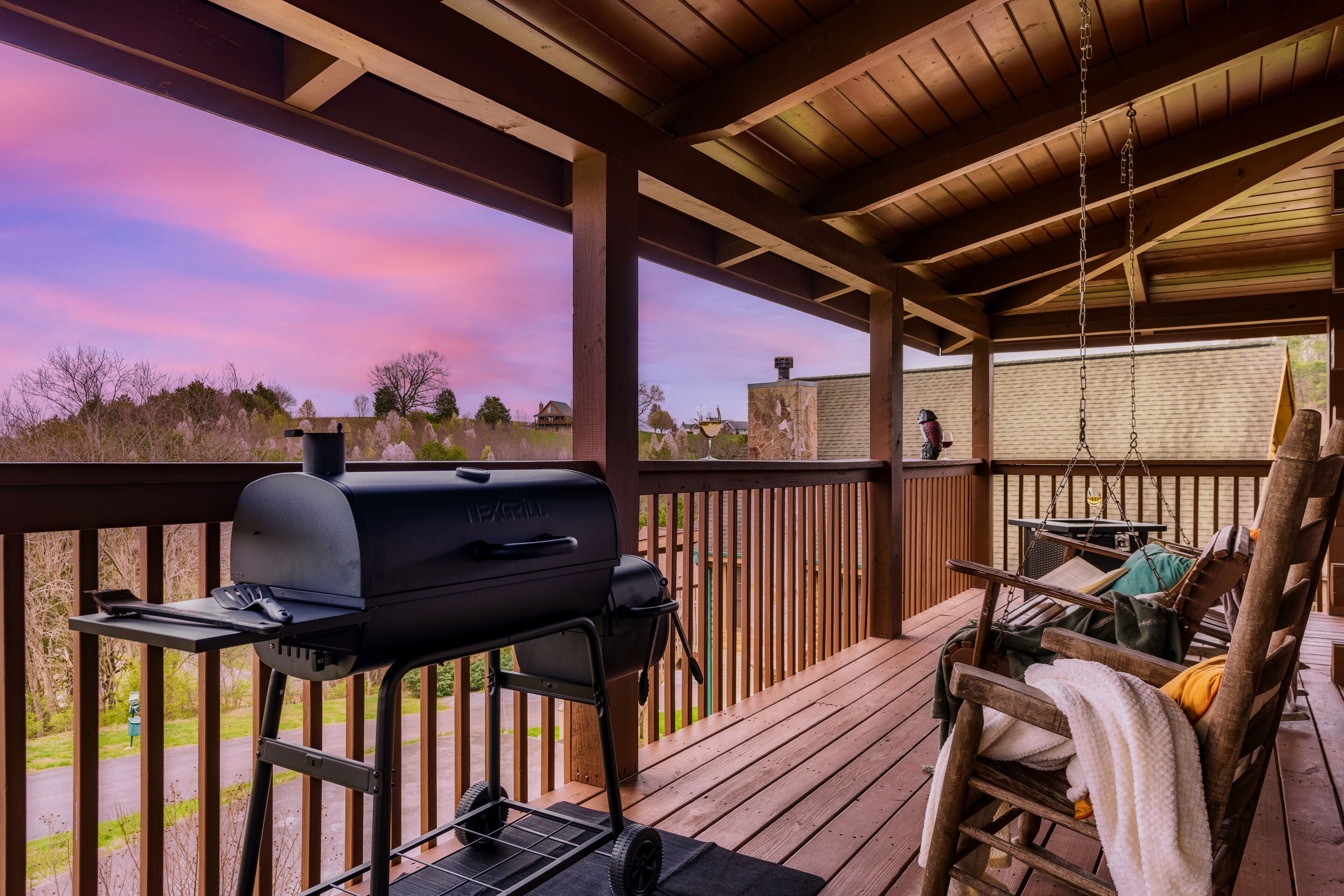 A covered deck with a grill, seating area, and a view of the landscape.
