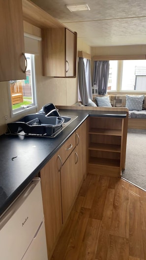 A compact kitchen with wooden cabinets, a black countertop, and a built-in sink. - Lovely 3-bed caravan  in beautiful north wales (Rhyl)