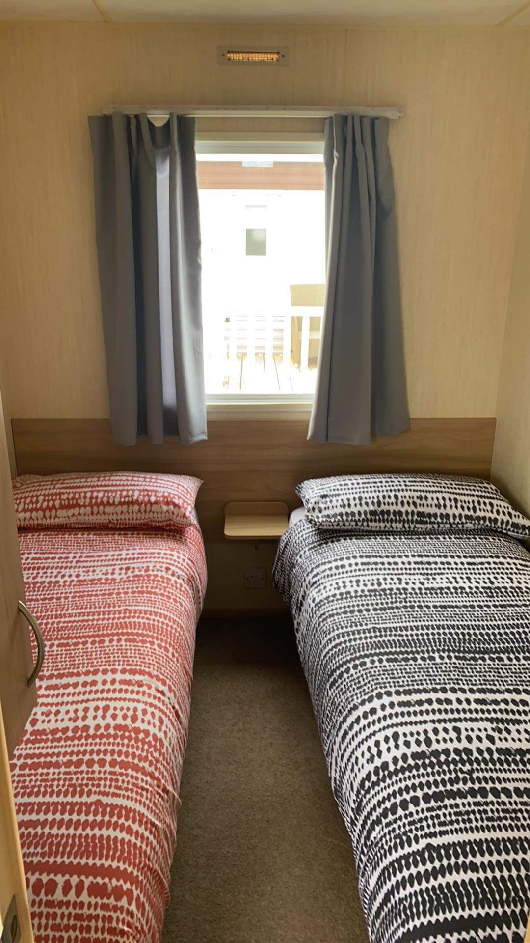 A compact room with two beds, a small table, and a window with curtains.