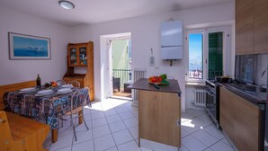 A compact kitchen with a dining area, a view through the open door, and a small island with fresh produce. - Dogana Best Lake View with Terrace, Torbole sul Garda, Italy (Torbole sul Garda)