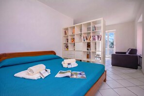 A hotel room with a bed, a bookshelf, a chair, and a window.
