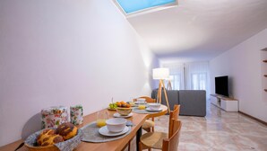 A dining area with a table set for breakfast, a television in the background, and a skylight above.