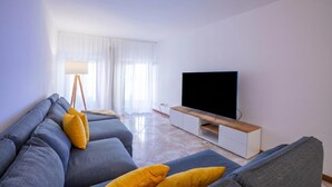 A modern living room with a sofa set, a flat-screen TV, and a floor lamp.