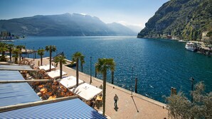 A waterfront hotel with outdoor seating, palm trees, and a view of a lake and mountains.