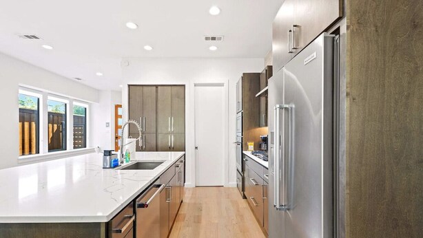 A modern kitchen with a large island, stainless steel appliances, and a view of the backyard through large windows.