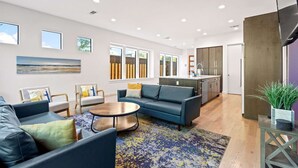 A modern living room with a blue sofa, a coffee table, and a rug. There is a kitchen area with cabinets and a sink.