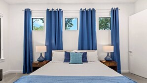 A bedroom with a large bed, two bedside tables with lamps, and blue curtains.