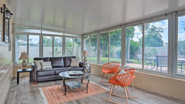 A sunlit room with a leather sofa, two rocking chairs, a coffee table, and a view of a backyard through large windows. - Colorful Fort Myers Home w/ Sunroom & Patio! (Fort Myers)