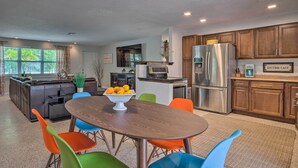 A modern kitchen with a dining area, featuring a wooden table, colorful chairs, and a bowl of fruit. - Colorful Fort Myers Home w/ Sunroom & Patio! (Fort Myers)