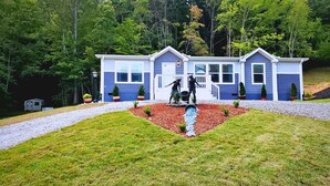 A two-story house with a front porch, a small garden with a statue, and a gravel driveway.