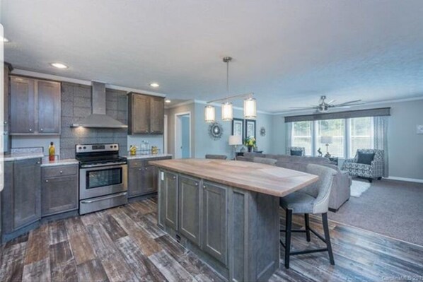 A modern kitchen with a central island, built-in appliances, and a dining area with a large window. - Enjoy this Beautiful Peaceful Mountain View home (Candler)