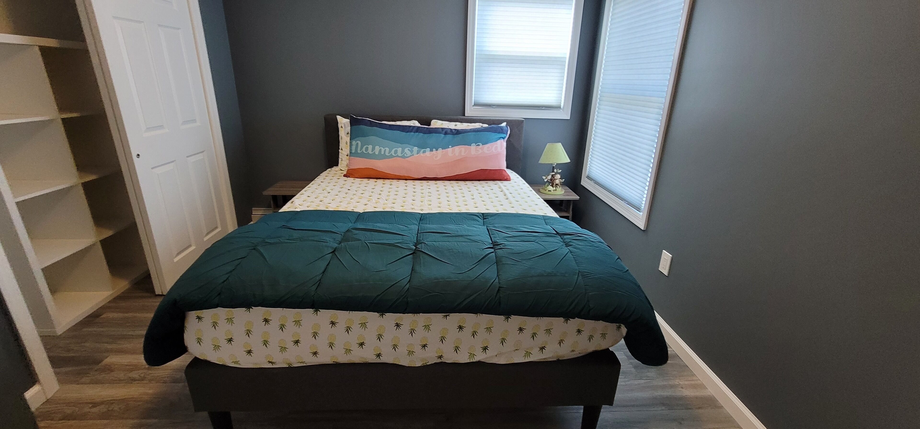 A bedroom with a bed, a nightstand, a lamp, a window with blinds, and a door to a closet.