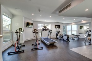 A modern gym with various exercise equipment, large windows, and a clean, spacious layout.