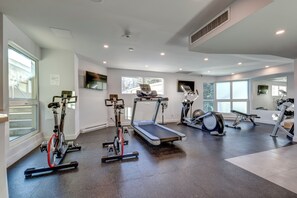 Une salle de sport moderne dotée de divers équipements d’exercice, de grandes fenêtres et d’un aménagement propre et spacieux.