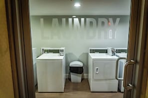 A laundry room with two washing machines and a dryer, a trash bin, and a toilet.