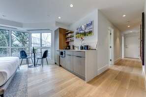 Een moderne slaapkamer met een groot bed, een eethoek met twee stoelen, en een keuken met een inbouwoven en magnetron.